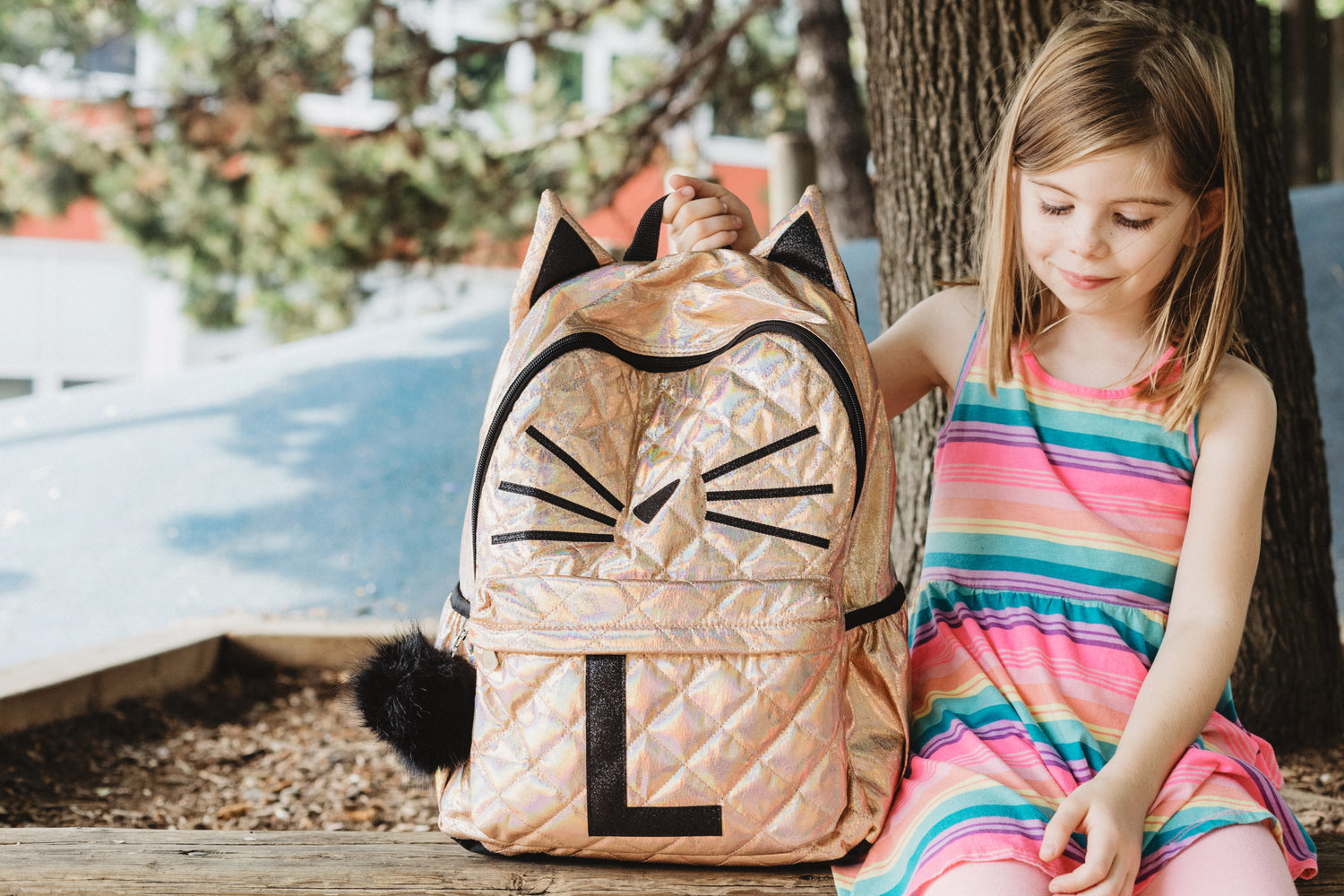 A young girls sitting down with a new backpack for school, the backpack has ears representing a cat